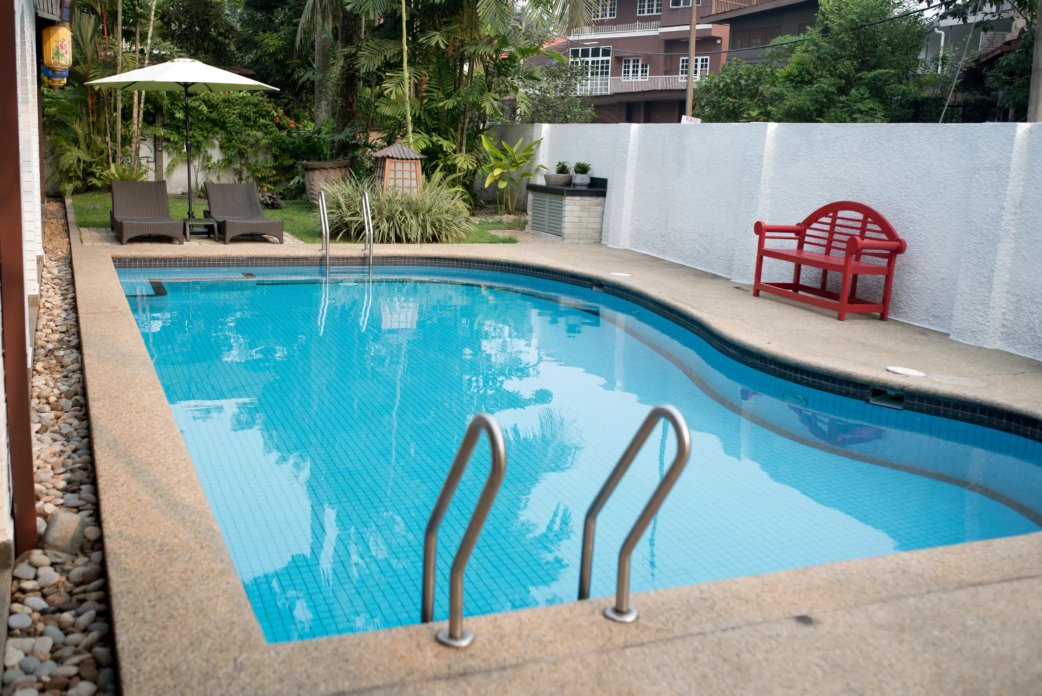 Backyard pool with loungers and red bench.