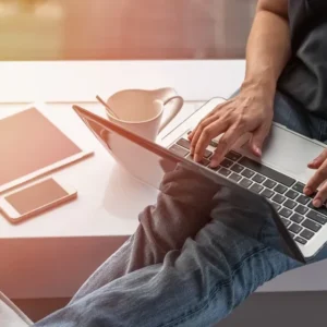 Person using laptop with coffee and smartphone nearby.