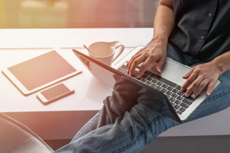 Person using laptop with coffee and smartphone nearby.